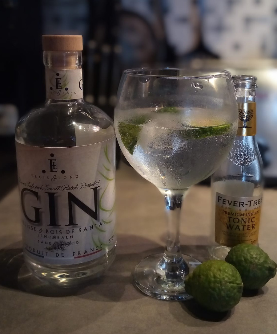 A serving of Lemon Balm & Sandalwood Gin in a large, ballon glass with ice and lemon.