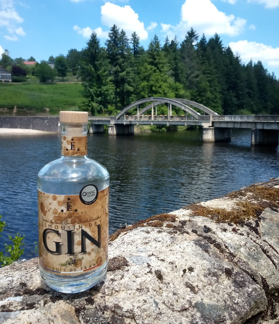 Une bouteille de Limousin Dry Gin posée sur un mur de pierre à Châtelus-le-Marcheix surplombant la rivière Taurion avec le pont en arrière-plan.
